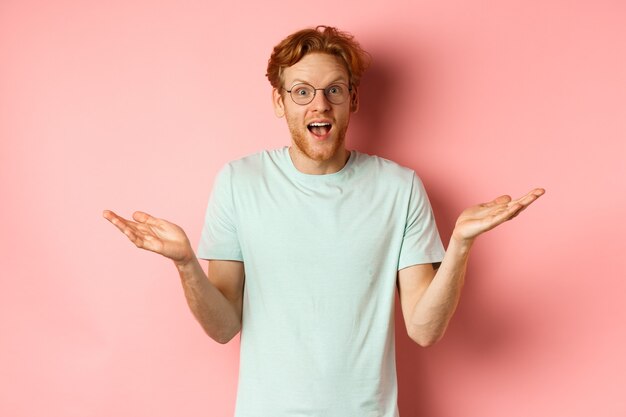Afbeelding van een verbaasde roodharige man met een bril die zijn handen zijwaarts spreidt en er onder de indruk uitziet terwijl hij voor hem staat.