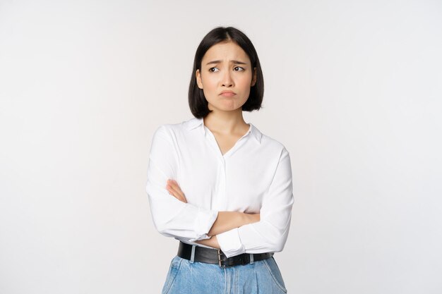 Afbeelding van een verdrietig kantoormeisje, een aziatische vrouw die mokkend en fronsend teleurgesteld staat, overstuur en bedroefd staat tegen een witte achtergrond