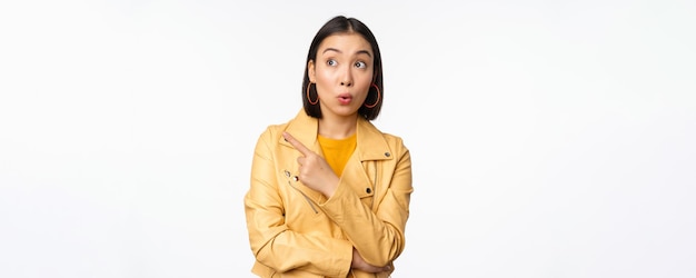 Afbeelding van een verraste aisan-vrouw die met de vinger naar links wijst en naar logo of banner kijkt met een geïntrigeerde gezichtsuitdrukking die op een witte achtergrond staat