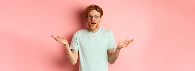 Gratis foto afbeelding van een verraste roodharige man met een bril die de handen zijwaarts spreidt en onder de indruk staat