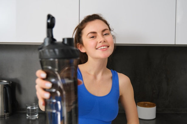 Afbeelding van fit en gezond glimlachende jonge vrouw die een fles water aanbiedt om je een drankje te geven na fitness