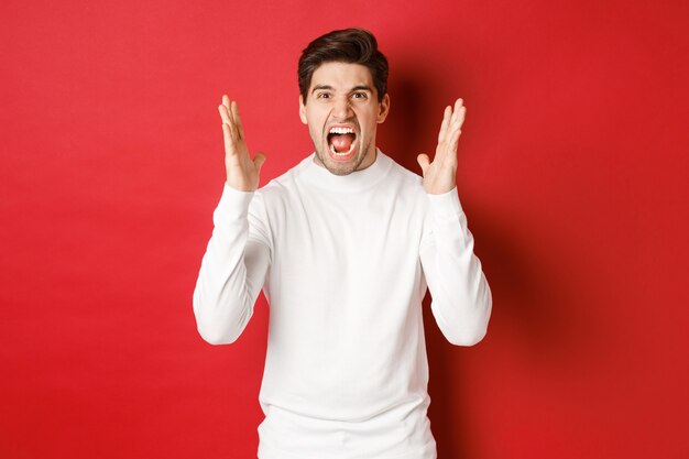 Afbeelding van gefrustreerde en boze man in witte trui die schreeuwt van woede en boos is op iemand die voorover staat...