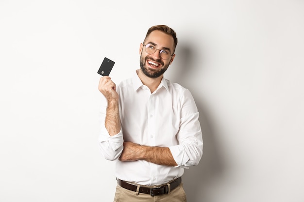 Afbeelding van knappe man na te denken over winkelen en creditcard vast te houden, nadenkend kijken naar de linkerbovenhoek