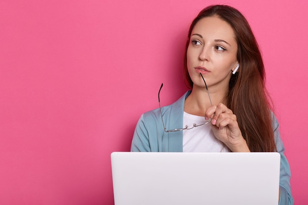 Afbeelding van peinzende vrouw poseren tegen roze muur.