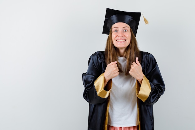 Afgestudeerde vrouw die winnaargebaar in vrijetijdskleding, uniform toont en gelukkig kijkt. vooraanzicht.