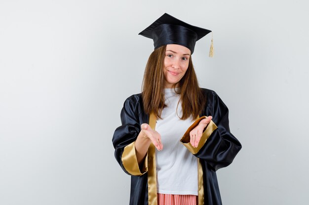 Afgestudeerde vrouw doet welkom gebaar in vrijetijdskleding, uniform en op zoek vrolijk. vooraanzicht.