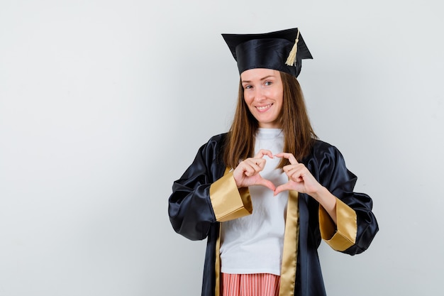 Afgestudeerde vrouw in vrijetijdskleding, uniform hartgebaar tonen en op zoek blij, vooraanzicht.