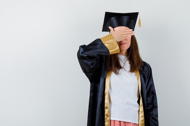 Afgestudeerde vrouw met de hand op de ogen in vrijetijdskleding, uniform en hoopvol op zoek. vooraanzicht.