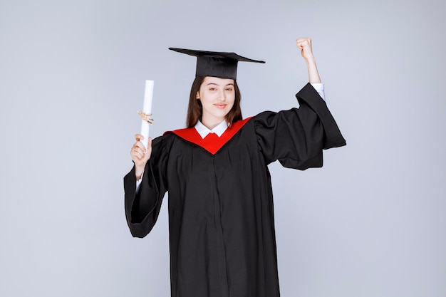 Afgestudeerde vrouwelijke student die haar diploma met duimen omhoog teken toont. Hoge kwaliteit foto