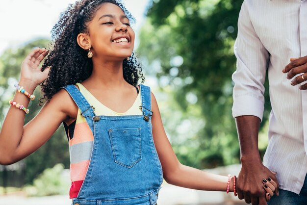 Afrikaans Amerikaans meisje geniet van een dag buiten met haar vader terwijl ze elkaars hand vasthouden en over straat lopen.