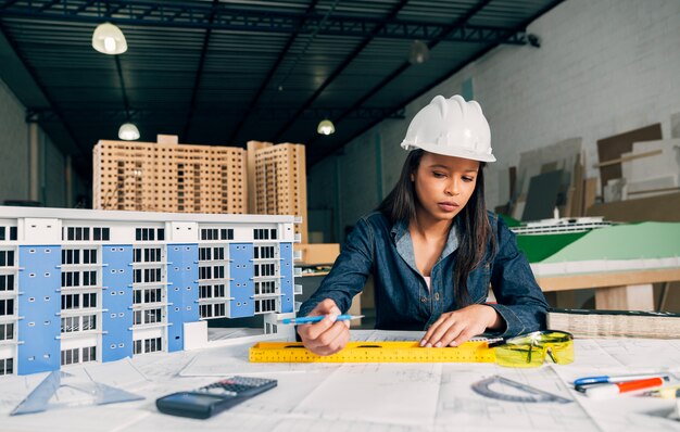 Afrikaans-Amerikaanse vrouw in veiligheidshelm die dichtbij model van de bouw werken