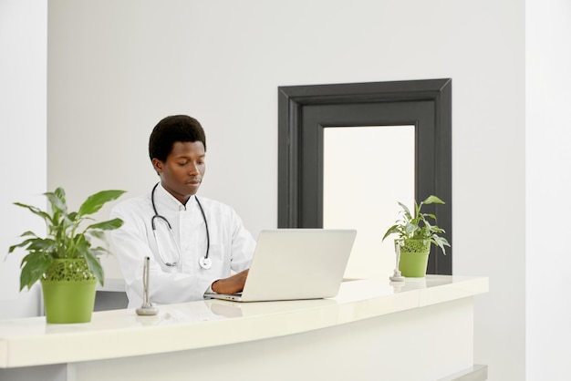 Afrikaanse arts in jas met laptop bij receptie