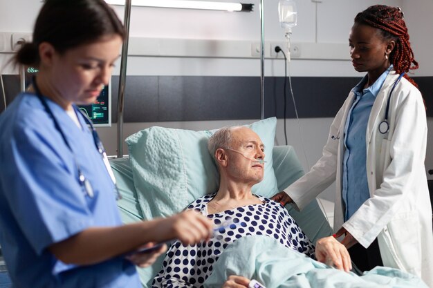 Afrikaanse arts in ziekenhuiskamer in gesprek met zieke senior man
