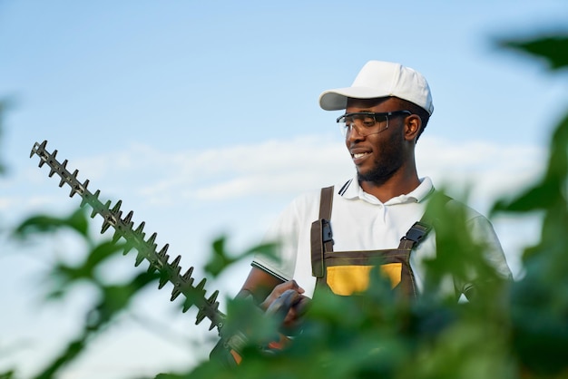 Gratis foto afrikaanse man in uniform aan het werk in de tuin met heggenschaar
