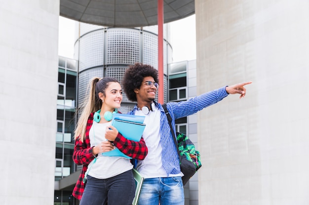 Afrikaanse mannelijke studenten die zich buiten de universiteit bevinden die iets tonen aan zijn vrouwelijke vriend