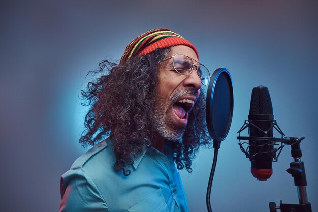 Afrikaanse Rastafari zanger man draagt een blauw shirt en muts die emotioneel een lied schrijft in de opnamestudio. Geïsoleerd op een blauwe achtergrond.