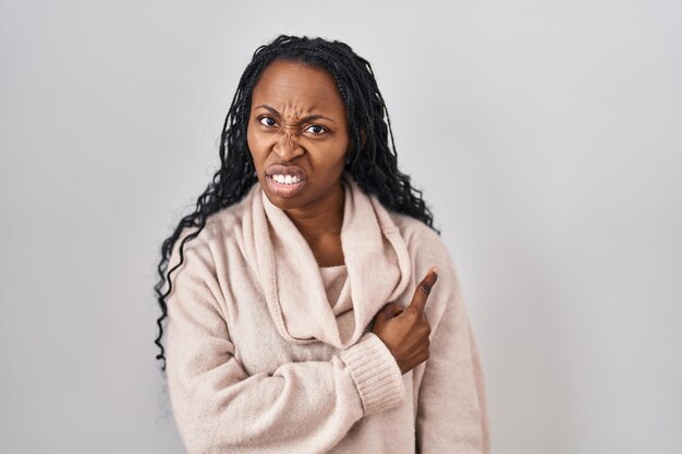 Afrikaanse vrouw die over een witte achtergrond staat en opzij wijst, bezorgd en nerveus met wijsvinger, bezorgde en verbaasde uitdrukking