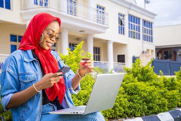 Afrikaanse vrouw zit buiten met haar laptop en telefoon online te betalen