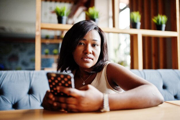 Afro-Amerikaans meisje zit in café met mobiele telefoon bij de hand