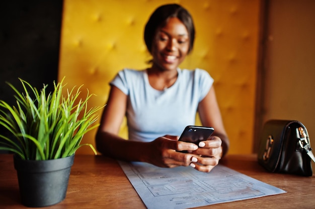 Afro-Amerikaans meisje zit in café met mobiele telefoon Zwarte vrouw die rust heeft