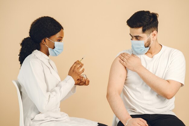 Afro-Amerikaanse arts die vaccin aan een man geeft. Beiden dragen maskers, geïsoleerd. Covid-19 vaccinatie.