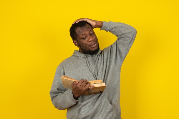 Afro-Amerikaanse denkende man die boeken in zijn hand leest, staat over gele muur.