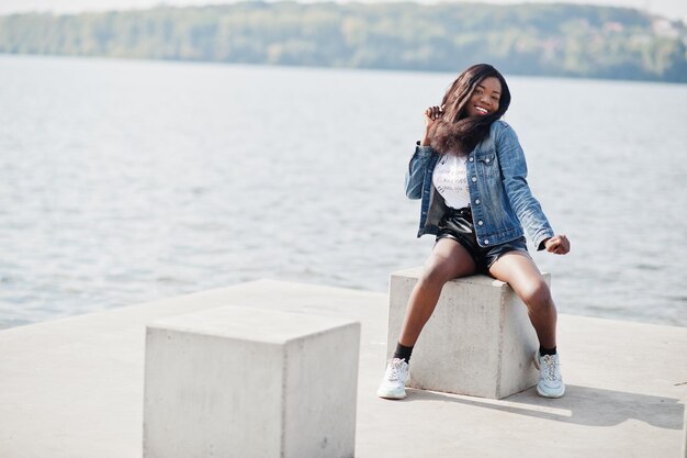 Afro-Amerikaanse donkere huid slank model poseerde in een zwarte korte broek en spijkerjasje tegen de zeezijde