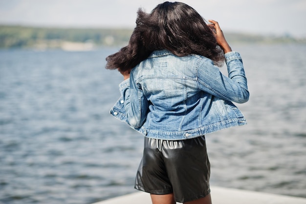 Afro-Amerikaanse donkere huid slank model poseerde in een zwarte korte broek en spijkerjasje tegen de zeezijde