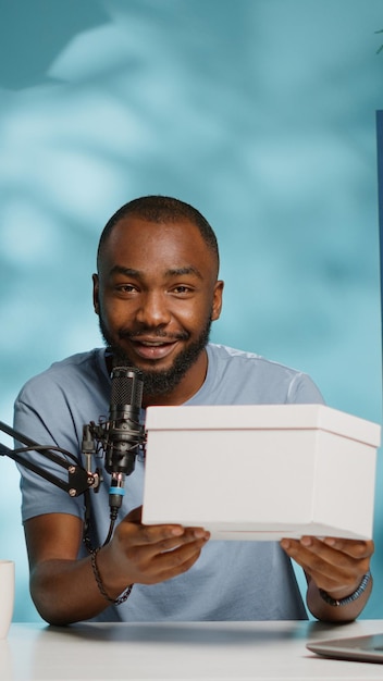 Afro-Amerikaanse influencer met huidige doos op camera voor online weggeefwedstrijd. Zwarte vlogger die video opneemt en cadeau toont om aan abonnees te geven voor inhoud op sociale media