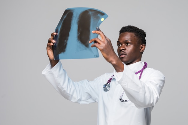 Afro Amerikaanse jonge dokter arts die röntgenstraal bekijkt die op grijze achtergrond wordt geïsoleerd