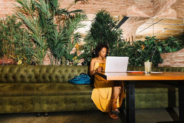 Gratis foto afro-amerikaanse jonge vrouw zitten in het restaurant met behulp van laptop