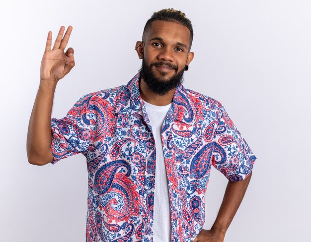 Afro-Amerikaanse jongeman in een kleurrijk shirt die naar de camera kijkt en vrolijk lacht met een goed teken