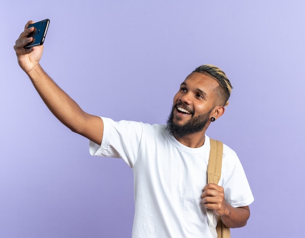 Afro-Amerikaanse jongeman in wit t-shirt doet selfie met smartphone happy
