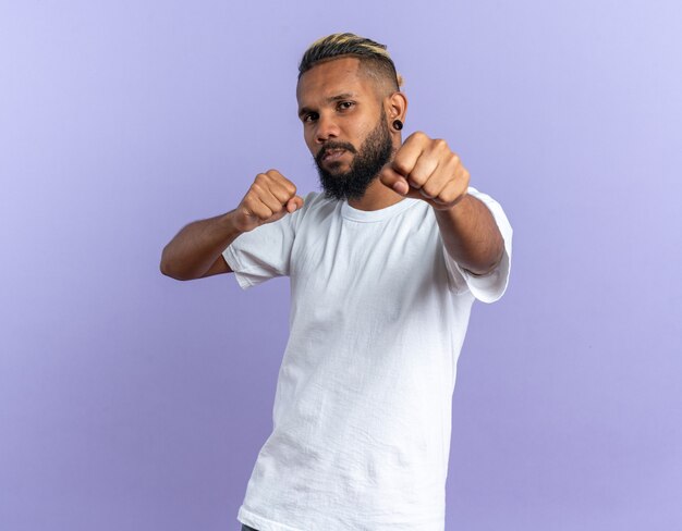 Afro-Amerikaanse jongeman in wit t-shirt kijkend naar camera glimlachend zelfverzekerd poserend met gebalde vuisten als een bokser