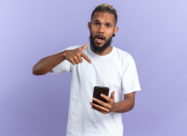 Afro-Amerikaanse jongeman in wit t-shirt met smartphone wijzend