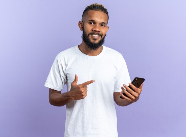 Afro-Amerikaanse jongeman in wit t-shirt met smartphone wijzend