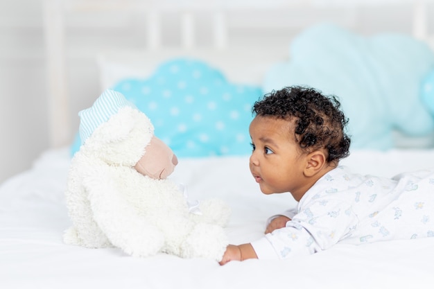 Afro-amerikaanse kleine baby in een wieg in de slaapkamer liggend op haar buik met een knuffel