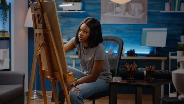 Afro-amerikaanse kunstenaar die het ontwerp van een witte vaas analyseert voor een tekenproject. zwarte jonge vrouw die authentieke inspiratie op canvas gebruikt om prachtig meesterwerk en kunstconcept te tekenen