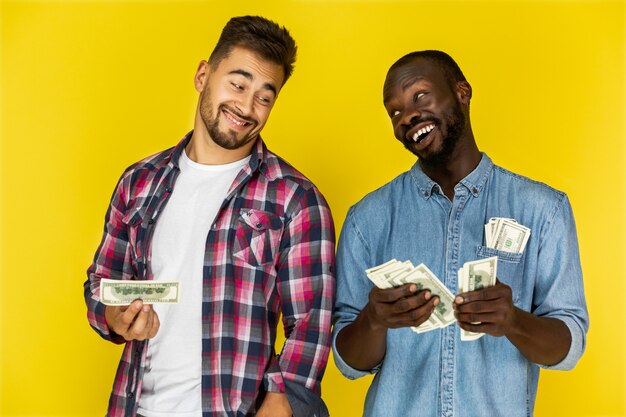 Afro-Amerikaanse man deelt geld met Europese man in informele kleding en beide lachen gelukkig