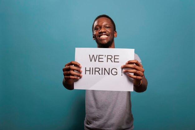 Afro-Amerikaanse man die op papier reclame maakt voor het inhuren van een baan, een baan aanbiedt voor een loopbaan in de human resources. Jonge werknemer die bericht gebruikt om sollicitatie met interview te maken.