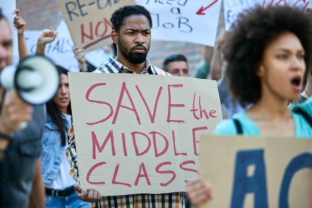 Afro-Amerikaanse man draagt een spandoek met het opschrift 'red de middenklasse' terwijl hij protesteert met een menigte mensen in de straten van de stad