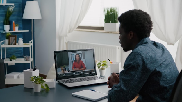 Afro-Amerikaanse man, externe werknemer die vanuit huis werkt, online kantooroproep neemt met partners en collega's en hen begroet. Computergebruiker vanuit thuiskantoor op video-internetconferentie via webcamconferentie