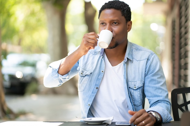 Afro-Amerikaanse man genieten van en drinken van een kopje koffie zittend in de coffeeshop buitenshuis