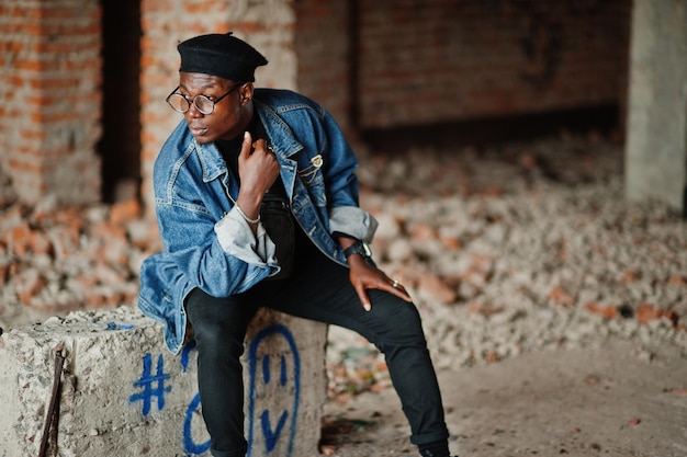 Afro-Amerikaanse man in jeans jas baret en bril bij verlaten steenfabriek