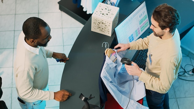 Afro-amerikaanse man koopt kleding bij de kassa van de winkel en gebruikt een kaart om transacties uit te voeren op de pos-terminal. winkelmedewerker die boodschappentassen geeft aan klant, commerciële activiteit. schot uit de hand.