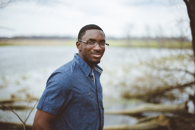 Gratis foto afro-amerikaanse man met een blauw shirt en een bril die zich overdag aan een meer bevindt