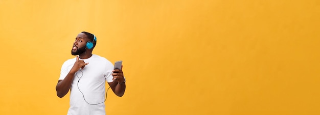 Afro-Amerikaanse man met koptelefoon luisteren en dansen met muziek geïsoleerd op gele achtergrond