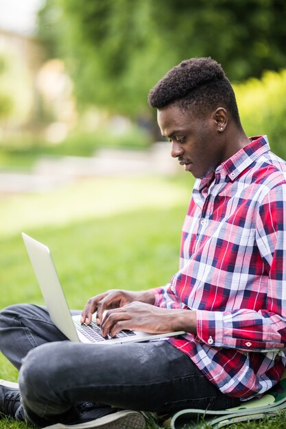 Afro-Amerikaanse man met laptop op het gras in stadspark