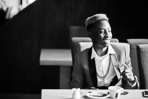 Afro-Amerikaanse man modemodel in rood pak met highlights haar zittend in café met koffie