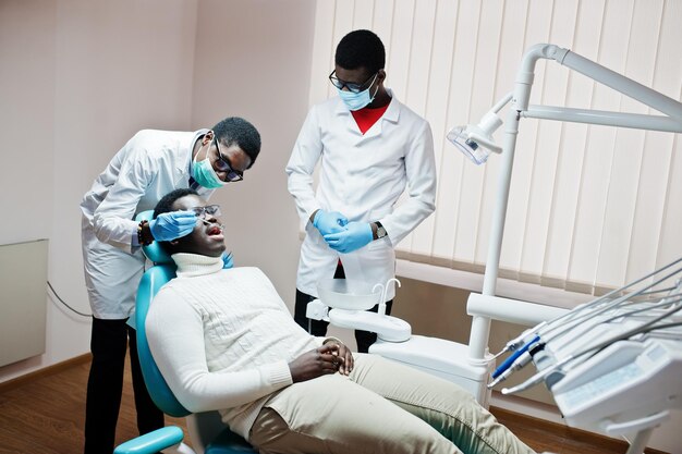 Afro-Amerikaanse man patiënt in tandartsstoel Tandarts kantoor en dokter praktijk concept Professionele tandarts helpt zijn patiënt bij tandheelkunde medisch